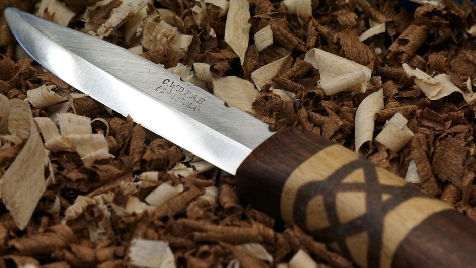 Detailed close-up of a carving knife with decorative handle amidst wood shavings.